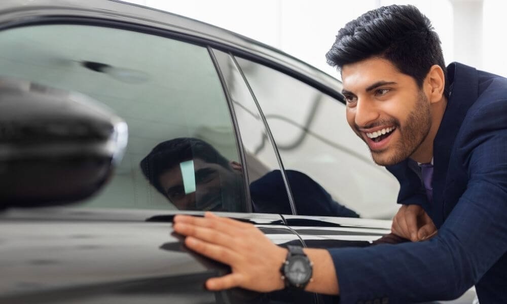 Excited man touching his brand new car after applying for New Car Loans